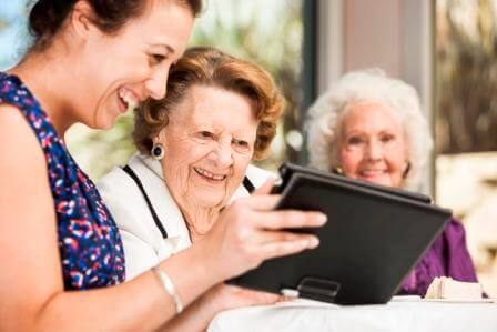 A Whiddon carer laughing with residents as they play with an iPad.