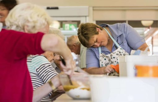A carer with residents baking in the kitchen as part of Whiddon's creative cooking program, VintageBites.