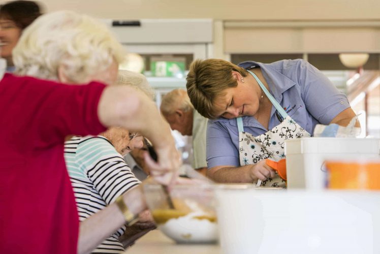 A carer with residents baking in the kitchen as part of Whiddon's creative cooking program, VintageBites.