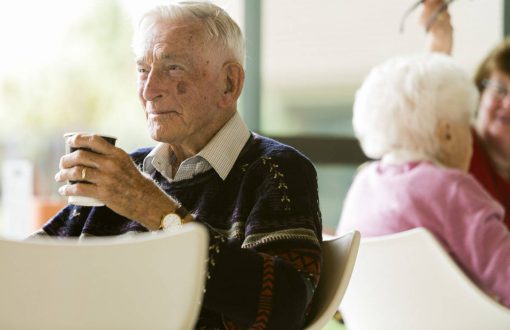 An elderly man enjoying a cup of coffee and pondering while looking into the distance.