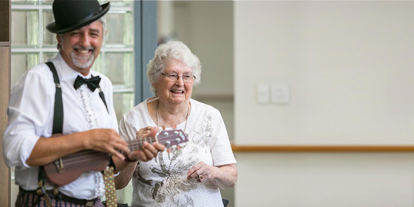 A resident dancing happily with Morrie who is playing a ukulele at Whiddon's nursing home in Maitland.