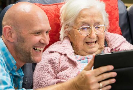A Whiddon carer laughing along with a resident as they play on an iPad at a community care home in Maitland.