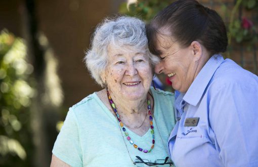 A carer smiling together with a resident at Whiddon's Glenfield aged care center.