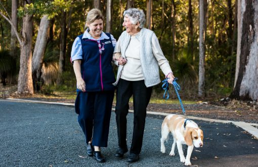 A Whiddon carer happily enjoying a stroll with a resident and a dog as part of Whiddon's Pet Therapy program.