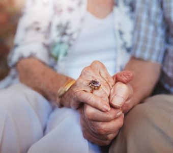 An elderly couple intimately holding hands.