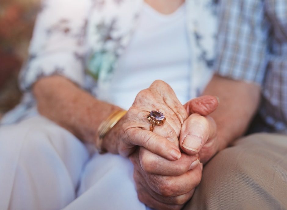An elderly couple intimately holding hands.