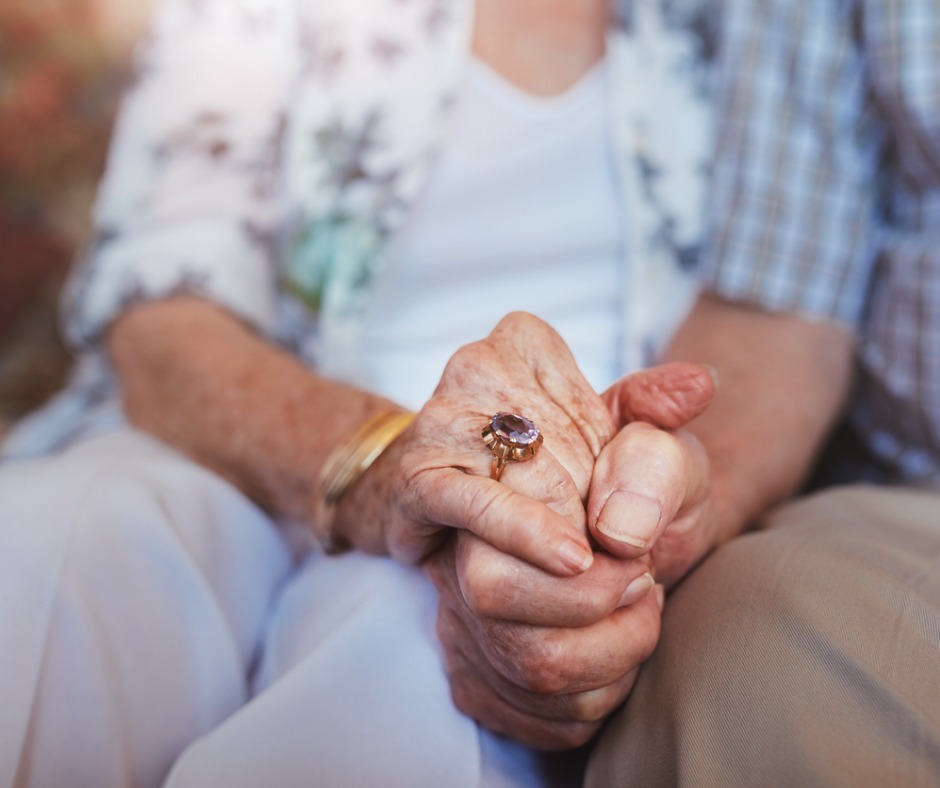 An elderly couple intimately holding hands.