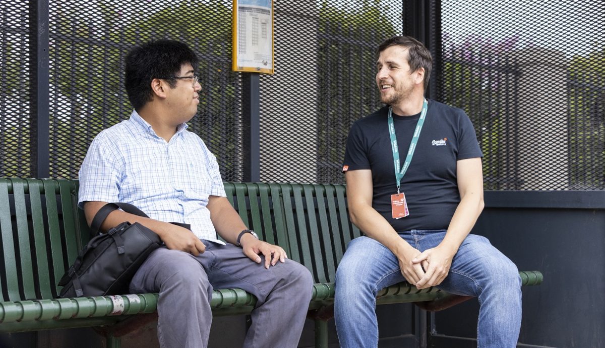 Disability participant, Chris is waiting for the bus at the bus stop with his carer, Andrew