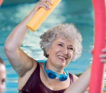 an older woman doing exercises with a noodle in the pool