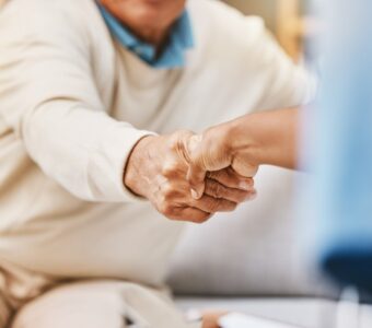 older adult shaking the hand of an aged care worker