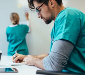 health care worker writing down notes on pad with coworker in background