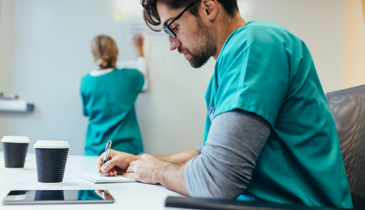 health care worker writing down notes on pad with coworker in background