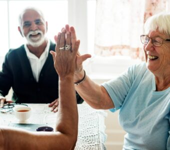 smiling older woman in aged care high-fiving another person