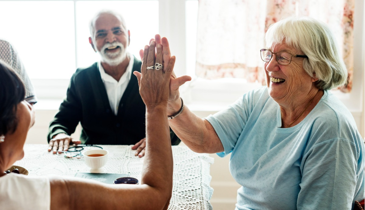smiling older woman in aged care high-fiving another person