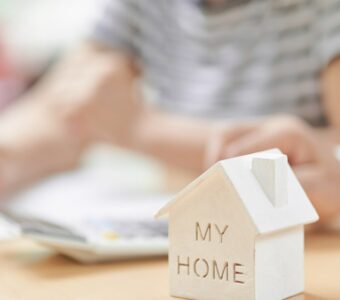 elderly couple signing document with model of their home in front of them