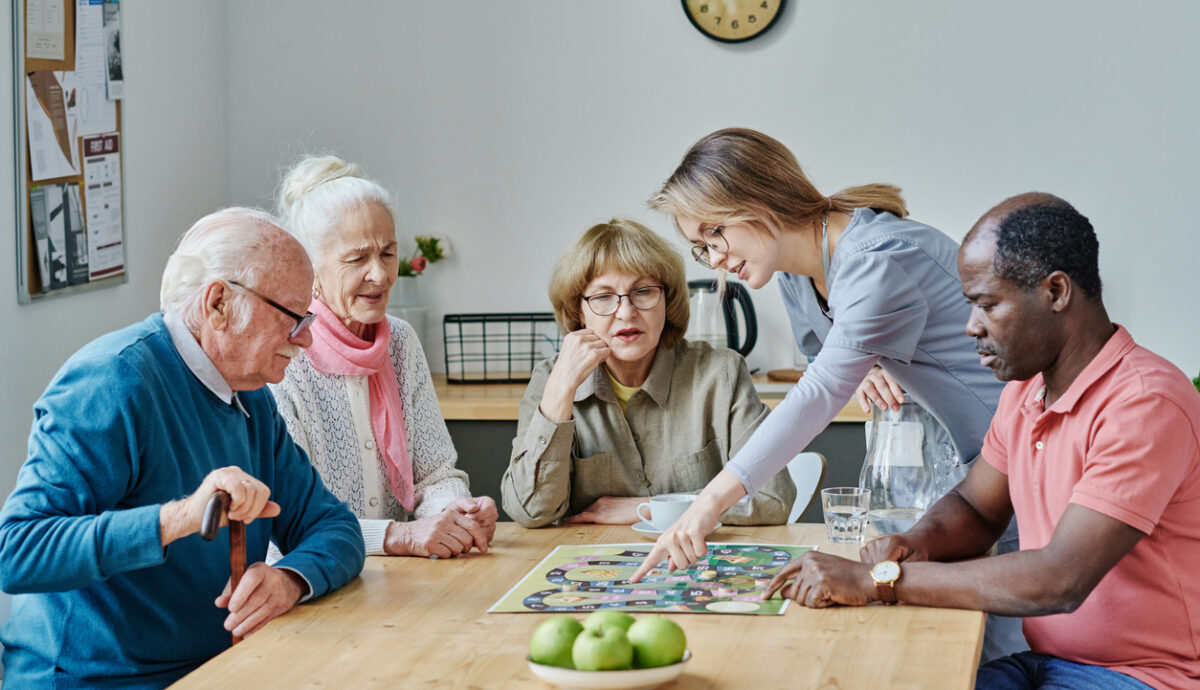 young aged care volunteer showing older adults a game