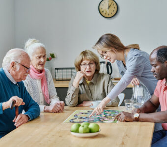 young aged care volunteer showing older adults a game