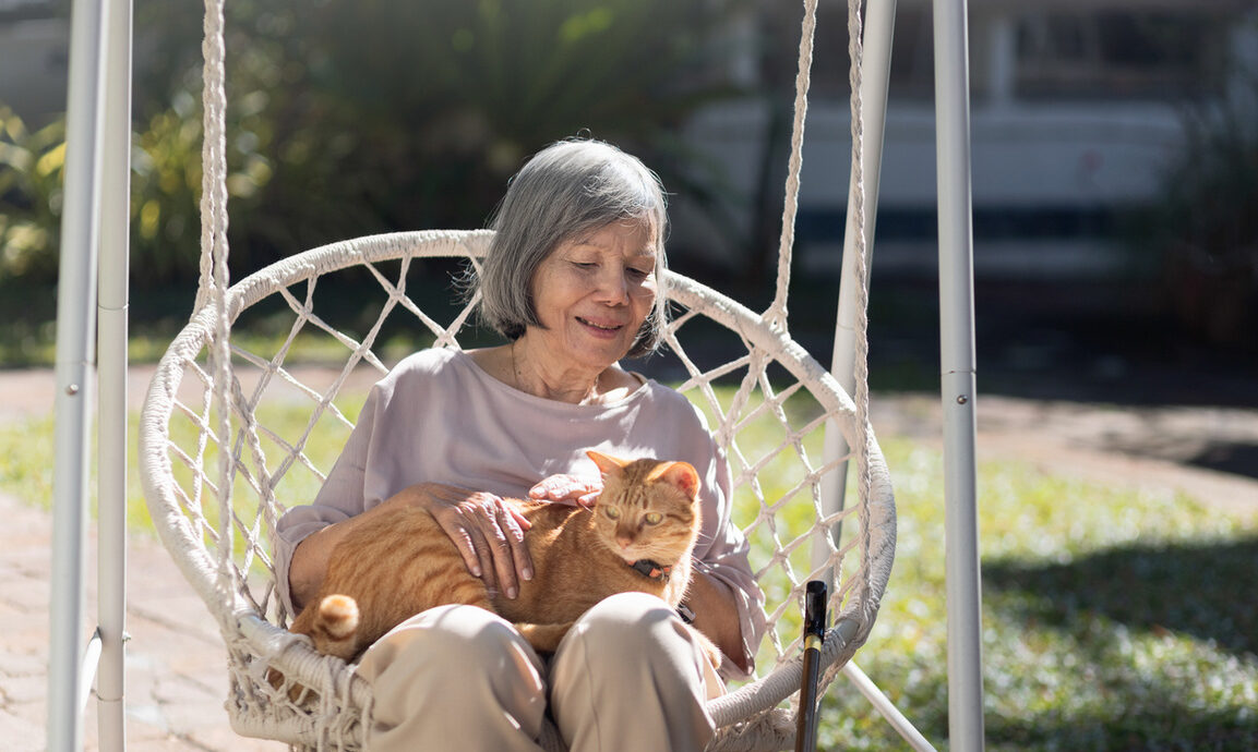 older woman petting a cat while sitting in backyard