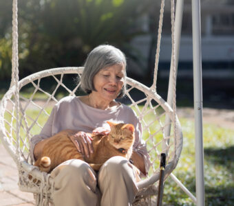 older woman petting a cat while sitting in backyard